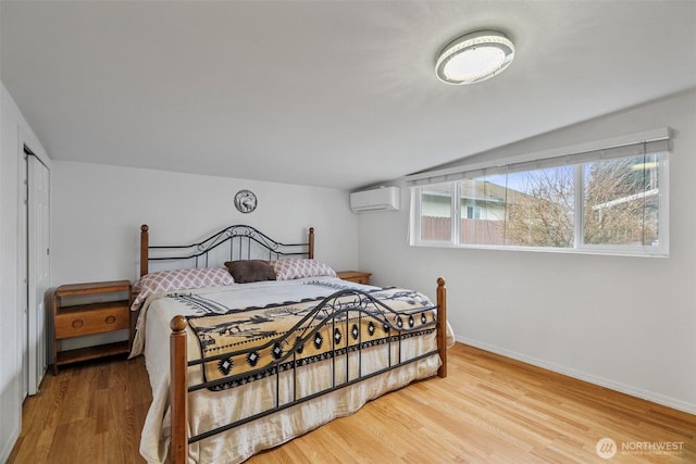 bedroom featuring a wall unit AC, wood finished floors, baseboards, and vaulted ceiling