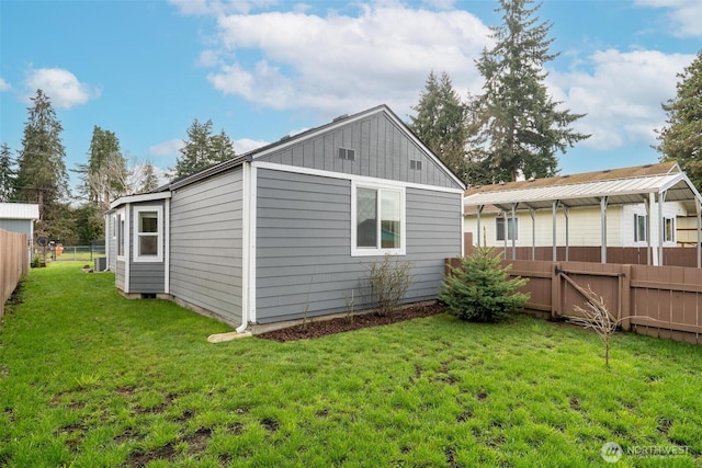 rear view of house with board and batten siding, fence, and a lawn