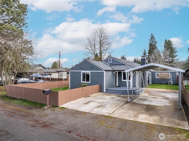 view of front of house with fence, a detached carport, concrete driveway, a shingled roof, and a chimney