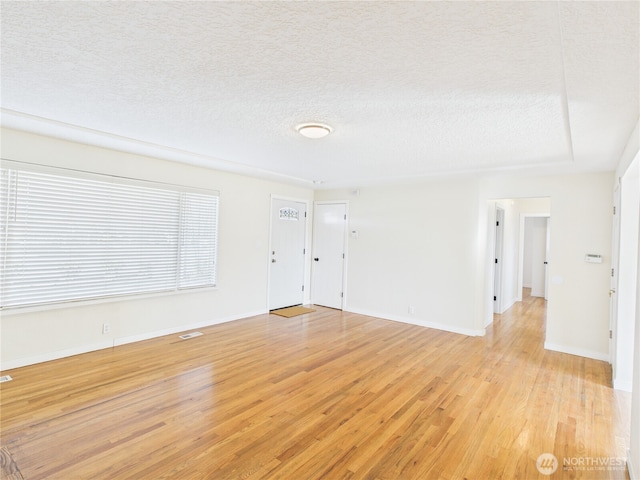 interior space featuring visible vents, baseboards, light wood-type flooring, and a textured ceiling