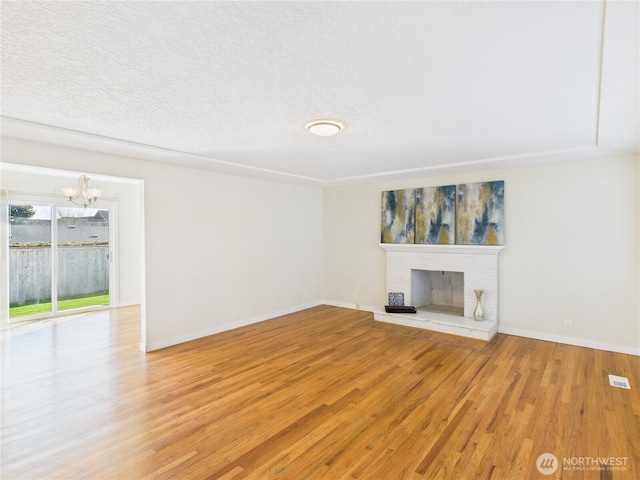 unfurnished living room featuring a textured ceiling, a brick fireplace, a chandelier, and light wood finished floors