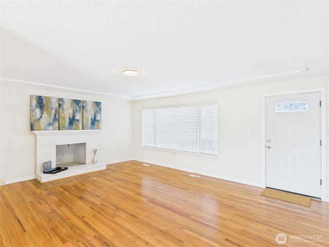 unfurnished living room featuring a textured ceiling, a fireplace, baseboards, and light wood-style floors