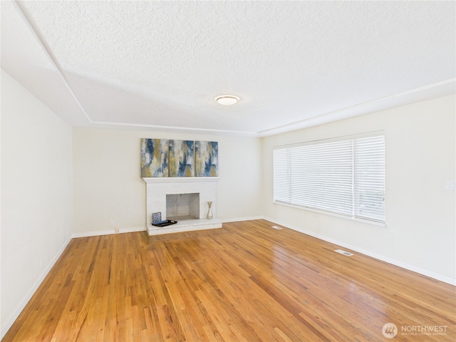 unfurnished living room featuring a brick fireplace, baseboards, light wood-type flooring, and a textured ceiling