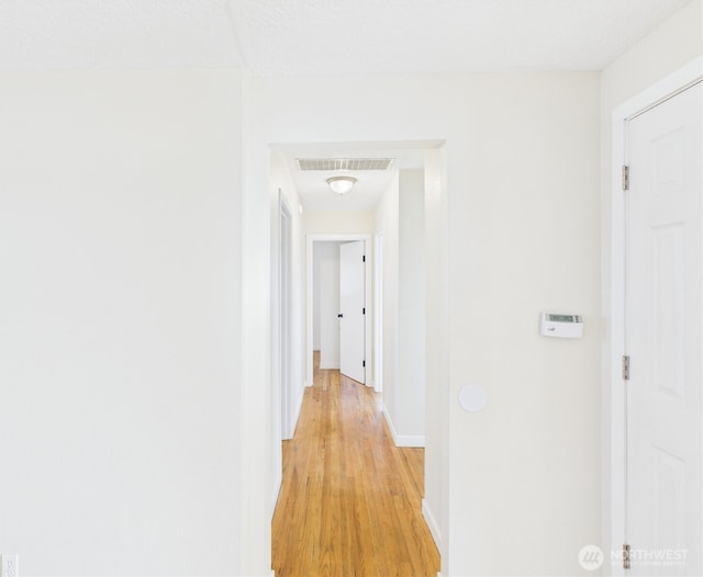 corridor featuring light wood-type flooring, visible vents, and baseboards