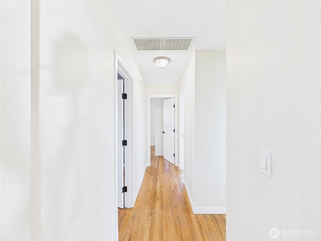 hallway with baseboards, visible vents, and light wood finished floors