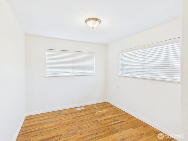 empty room featuring visible vents, light wood-type flooring, and baseboards