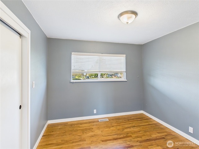 spare room featuring a textured ceiling, wood finished floors, visible vents, and baseboards