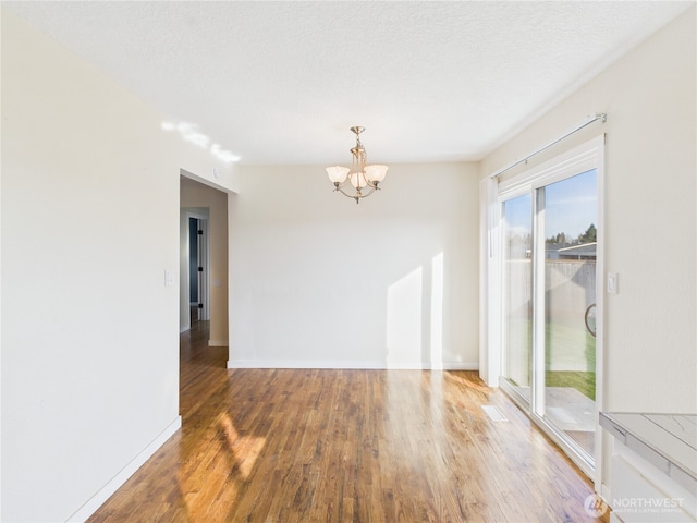 spare room featuring baseboards, a notable chandelier, wood finished floors, and a textured ceiling