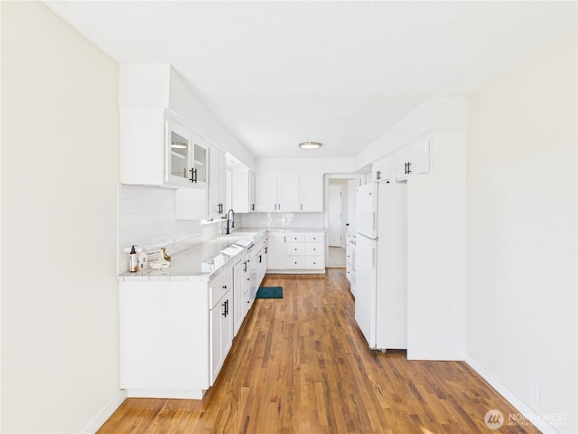 kitchen with a sink, tasteful backsplash, wood finished floors, freestanding refrigerator, and light countertops