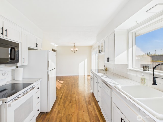 kitchen with tasteful backsplash, a chandelier, white appliances, white cabinetry, and a sink