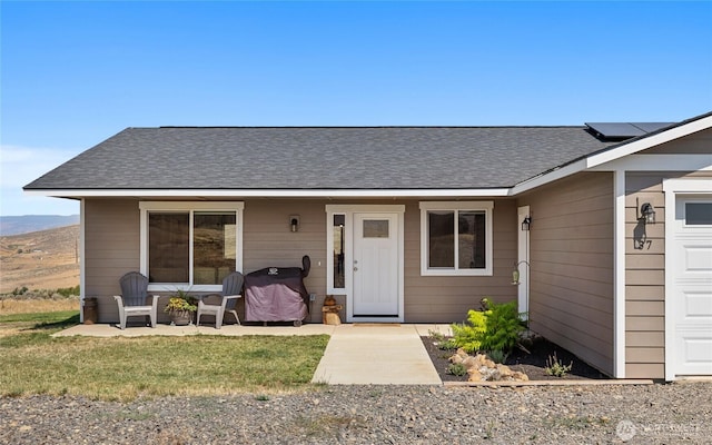 view of front of home featuring a garage, roof mounted solar panels, and a shingled roof