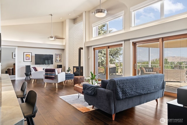 living room with high vaulted ceiling, hardwood / wood-style flooring, baseboards, ceiling fan, and a wood stove