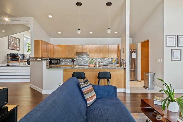 kitchen with under cabinet range hood, tasteful backsplash, freestanding refrigerator, wood-type flooring, and a peninsula