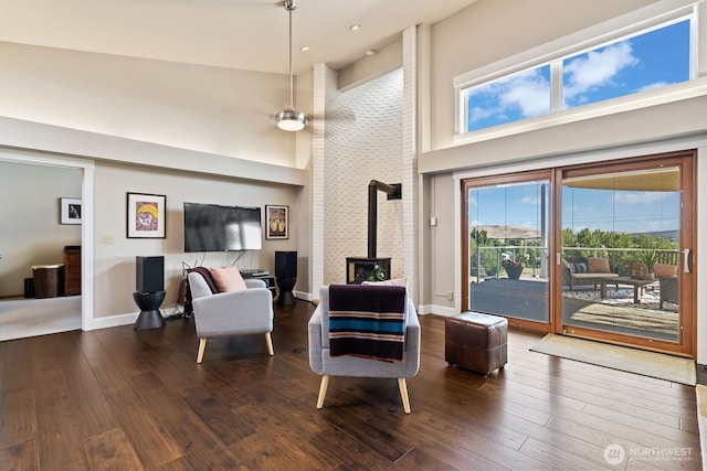 living area featuring baseboards, dark wood-type flooring, a towering ceiling, and a wood stove