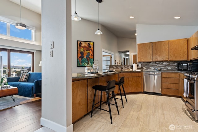 kitchen featuring brown cabinets, a breakfast bar, stainless steel appliances, dark countertops, and tasteful backsplash