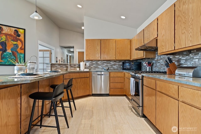 kitchen featuring decorative backsplash, vaulted ceiling, under cabinet range hood, appliances with stainless steel finishes, and a kitchen breakfast bar