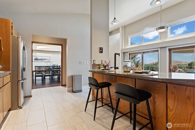 bar featuring decorative light fixtures, baseboards, freestanding refrigerator, and a towering ceiling