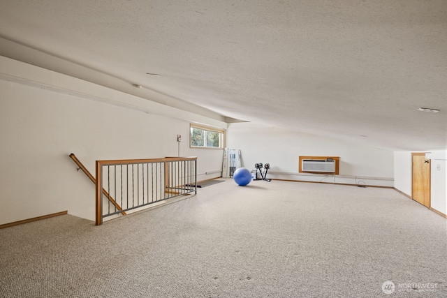 interior space with a textured ceiling, a wall mounted AC, baseboards, and carpet floors