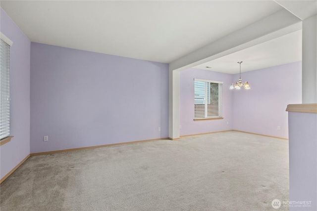 carpeted empty room with baseboards and a chandelier