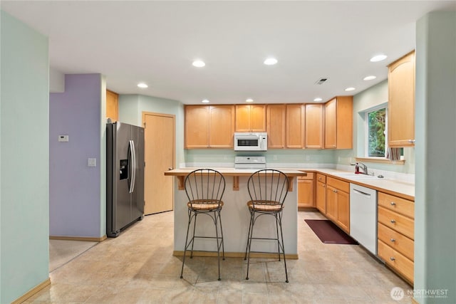 kitchen with light brown cabinets, a sink, a kitchen breakfast bar, white appliances, and light countertops