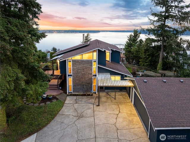 exterior space with a deck with water view, roof with shingles, and a patio area