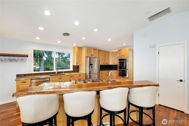 kitchen with light brown cabinetry, visible vents, stainless steel appliances, and a sink