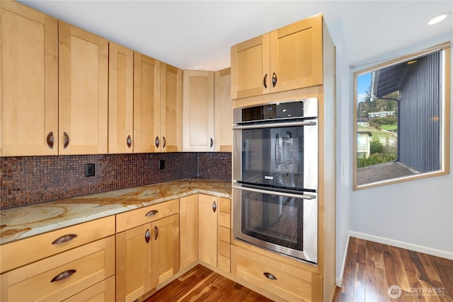 kitchen with stainless steel double oven, dark wood-type flooring, tasteful backsplash, and light brown cabinetry