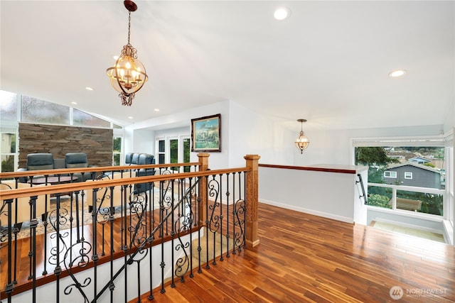 hallway with an upstairs landing, a chandelier, plenty of natural light, and wood finished floors