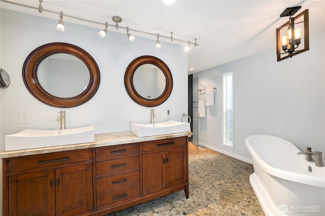 full bath with a sink, a freestanding tub, baseboards, and double vanity