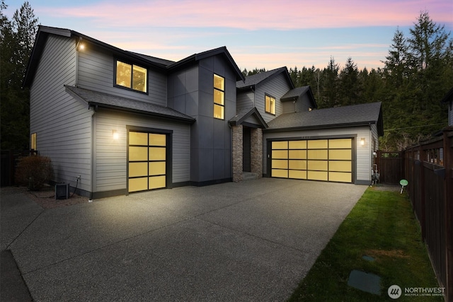 modern home with concrete driveway, an attached garage, fence, and central AC