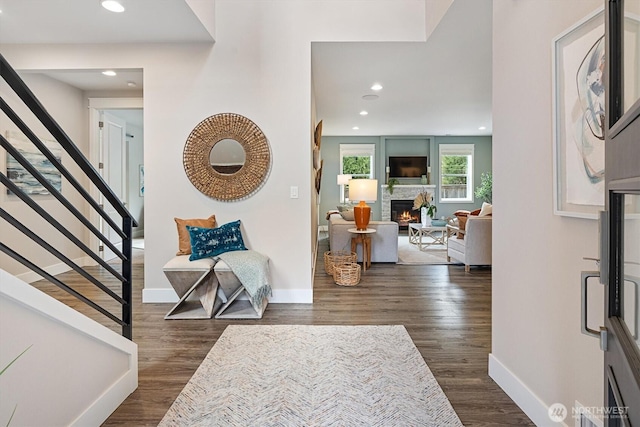 foyer entrance with baseboards, dark wood finished floors, stairway, recessed lighting, and a warm lit fireplace