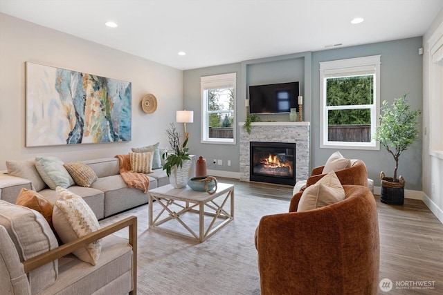 living room with a stone fireplace, recessed lighting, wood finished floors, and baseboards