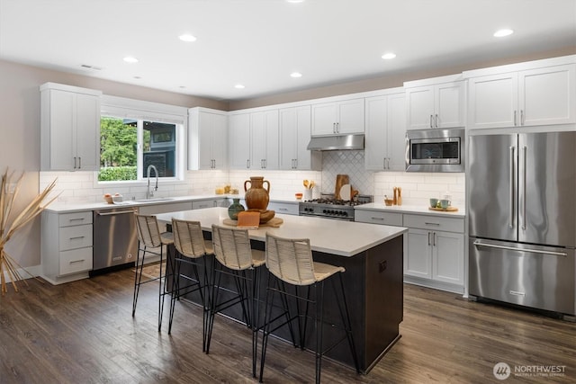 kitchen with dark wood-type flooring, under cabinet range hood, a breakfast bar area, high quality appliances, and a sink