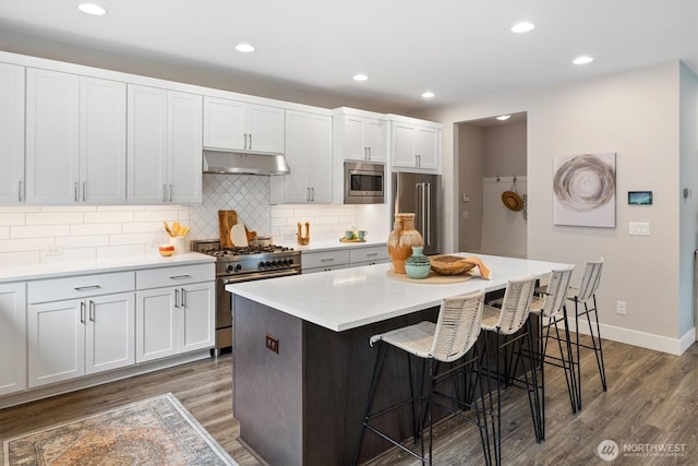 kitchen featuring under cabinet range hood, high quality appliances, a kitchen bar, and wood finished floors