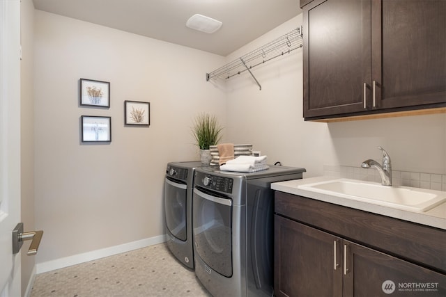 clothes washing area with a sink, baseboards, cabinet space, and separate washer and dryer