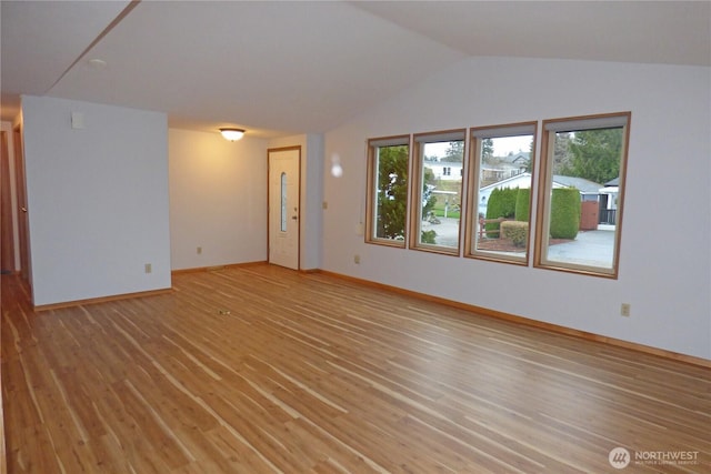 empty room with light wood finished floors, baseboards, and lofted ceiling