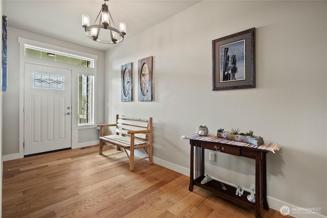 entryway with light wood-style flooring, a notable chandelier, and baseboards