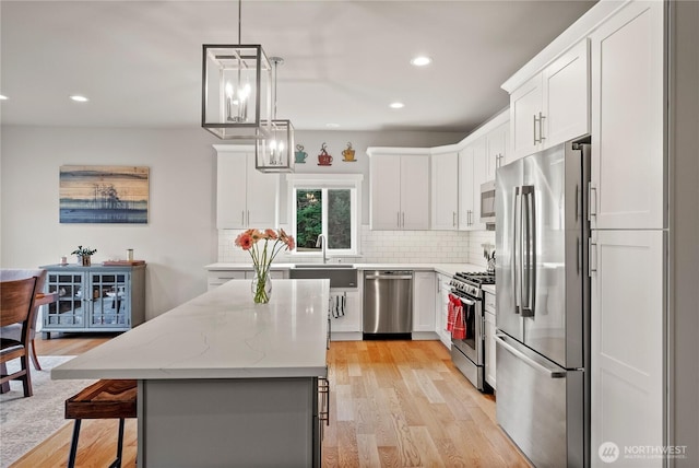 kitchen with light wood-style flooring, backsplash, a kitchen island, white cabinetry, and appliances with stainless steel finishes