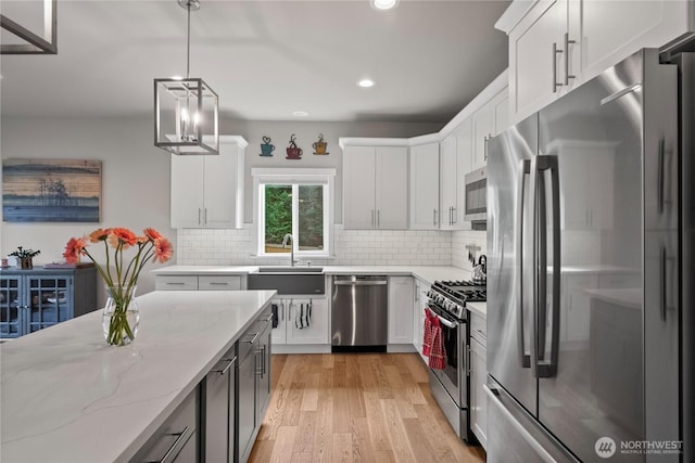 kitchen featuring light wood-type flooring, a sink, light stone counters, stainless steel appliances, and decorative backsplash