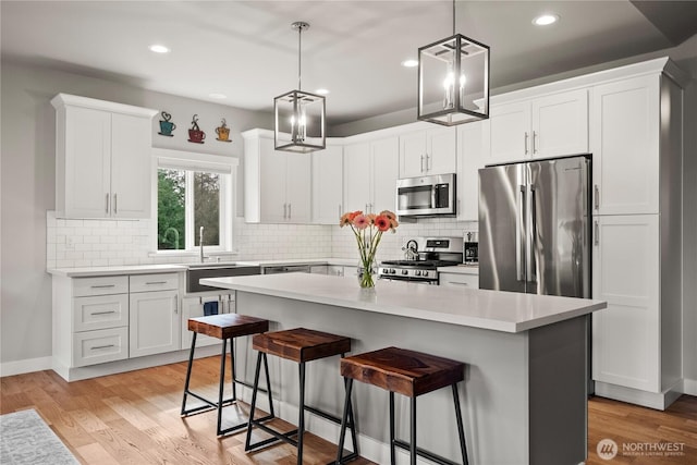 kitchen featuring light wood-type flooring, a sink, a kitchen island, appliances with stainless steel finishes, and a breakfast bar area