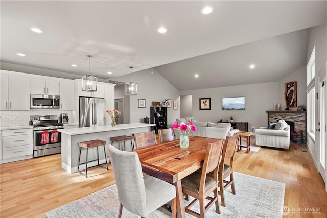 dining room featuring a stone fireplace, recessed lighting, light wood-style floors, and vaulted ceiling