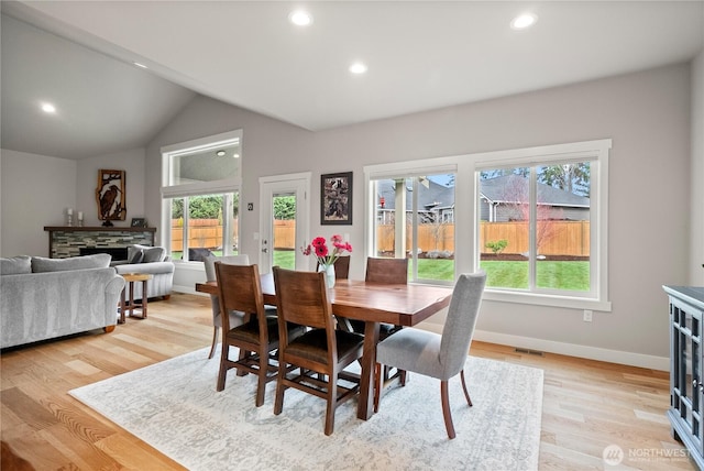 dining area with visible vents, lofted ceiling, light wood-style flooring, a stone fireplace, and baseboards