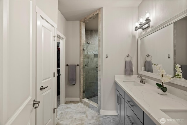 full bath featuring baseboards, double vanity, a sink, a shower stall, and marble finish floor