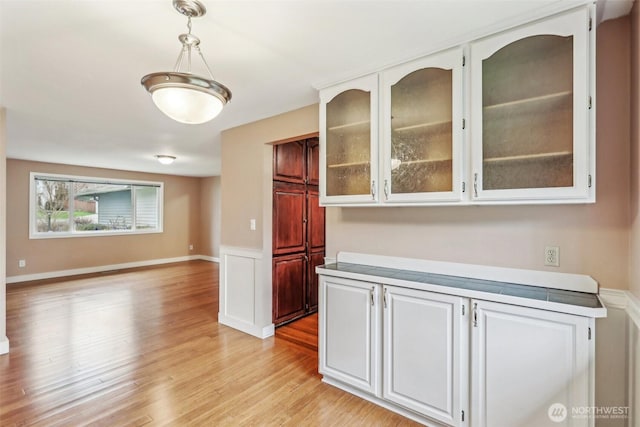 kitchen featuring light countertops, white cabinets, glass insert cabinets, and light wood-type flooring