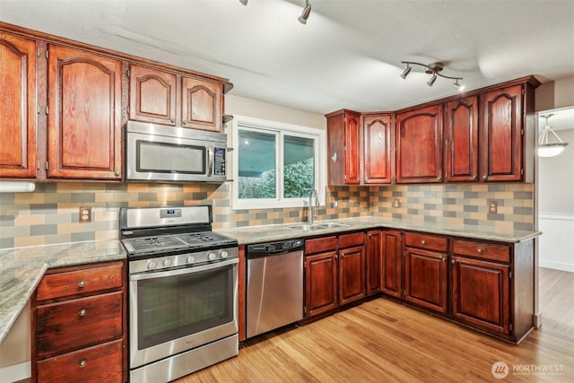 kitchen featuring a sink, light stone counters, light wood-style floors, appliances with stainless steel finishes, and decorative backsplash