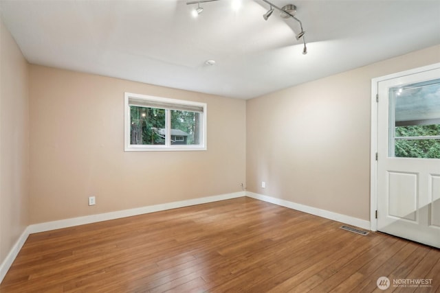 unfurnished room featuring hardwood / wood-style flooring, rail lighting, baseboards, and visible vents