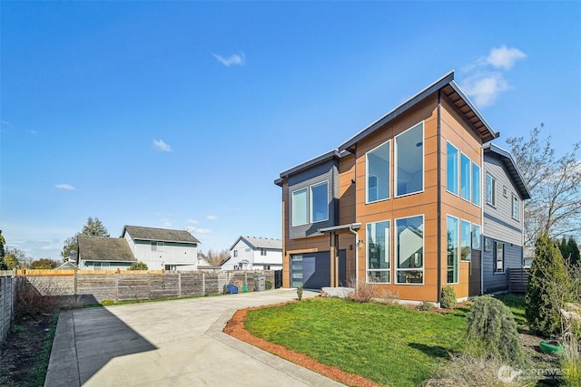 back of house featuring a lawn, an attached garage, concrete driveway, and fence