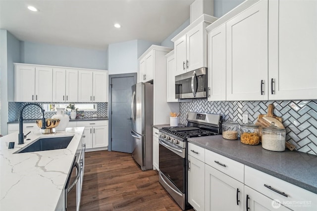 kitchen with light stone countertops, dark wood-style floors, white cabinets, stainless steel appliances, and a sink