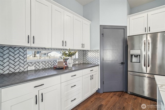 kitchen with dark wood-type flooring, stainless steel refrigerator with ice dispenser, dark countertops, tasteful backsplash, and white cabinets