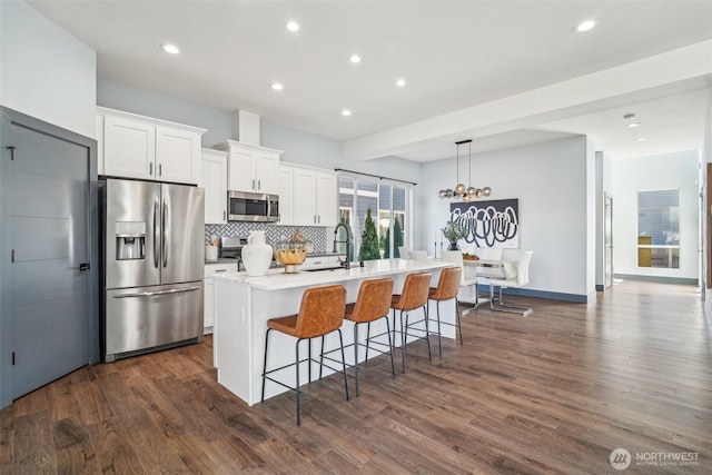 kitchen featuring dark wood-style floors, tasteful backsplash, appliances with stainless steel finishes, and an island with sink